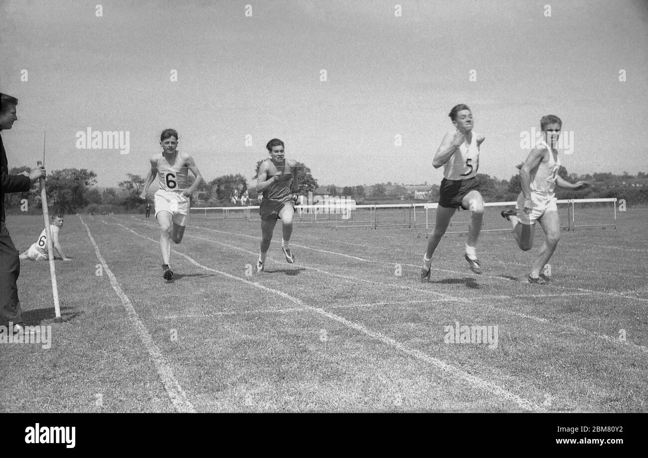 Scuola secondaria estate sport Day, Inghilterra, c1960, studenti senior in gara di corsa sprint e fare un ultimo sforzo prima di colpire il nastro finale tenuto accanto alla pista di erba da un compagno di scuola. Foto Stock