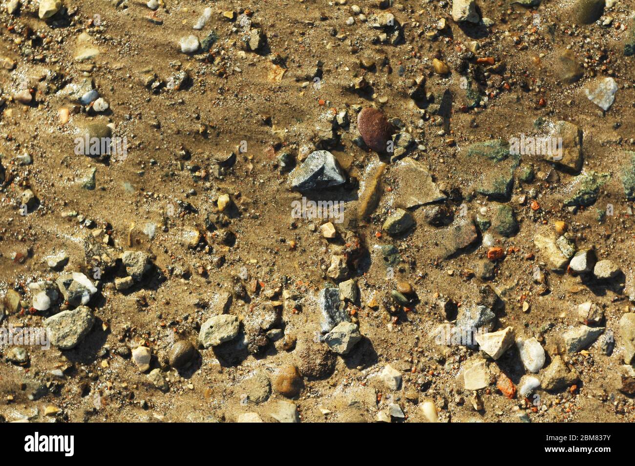 Piccole pietre e sabbia. La struttura naturale del suolo. Riva di un bacino idrico con una spiaggia e ciottoli. Foto Stock