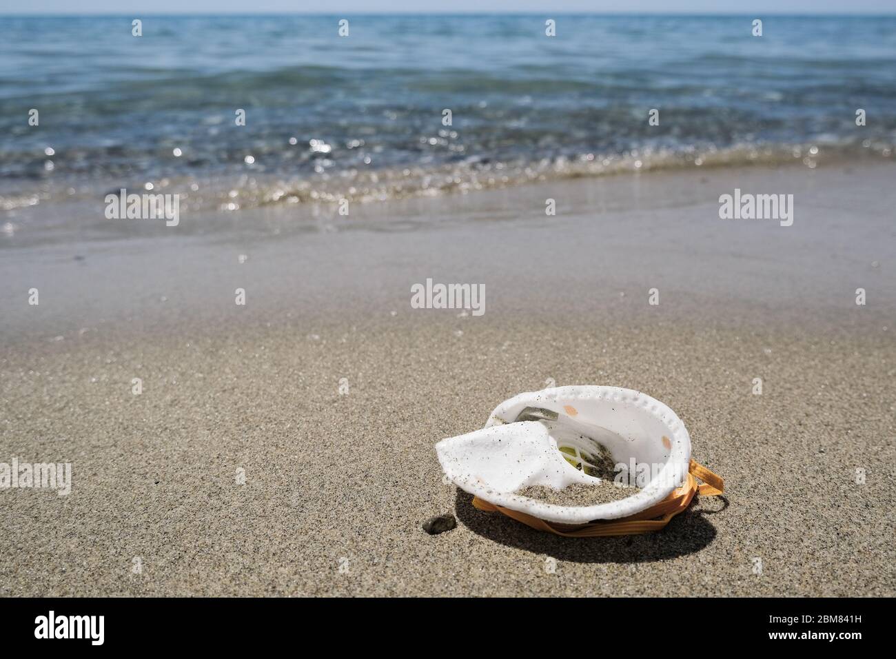 Maschera protettiva virus spazzatura spazzatura sulla spiaggia sabbiosa del mare, malattia di inquinamento del coronavirus Foto Stock