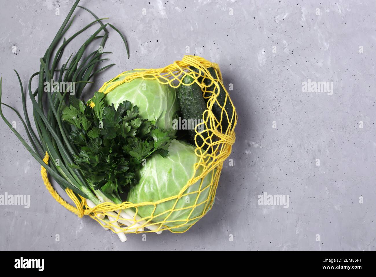 Sacco riutilizzabile a stringa in rete gialla con verdure verdi su fondo grigio in cemento. Concetto senza plastica, vista dall'alto, spazio di copia Foto Stock