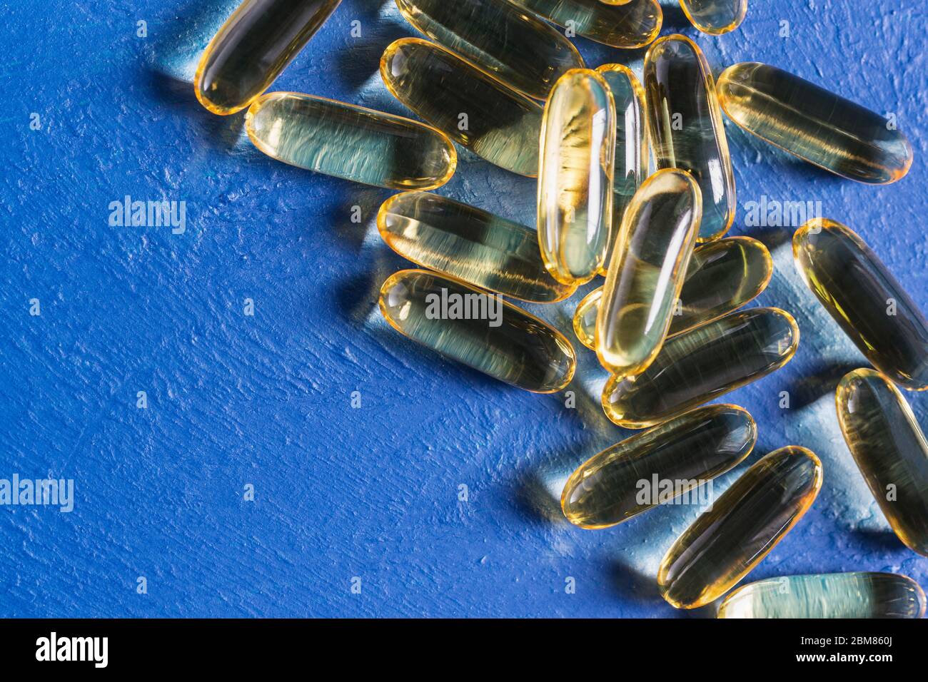 Capsule trasparenti di gelatina con olio di pesce giacciono su una superficie blu testurizzata. Acidi grassi polinsaturi Omega-3-essenziali Foto Stock