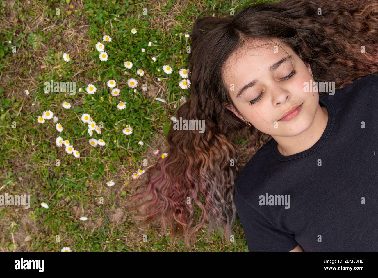 Ragazza bruna carina con capelli ricci e sciolti si trova a terra con occhi chiusi Foto Stock