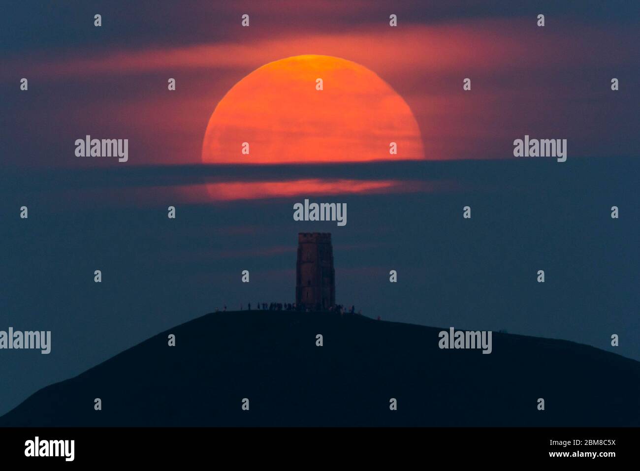 Glastonbury, Somerset, Regno Unito. 7 maggio 2020. Meteo Regno Unito. La luna piena si erge da dietro Glastonbury Tor nel Somerset ma è parzialmente oscurata dalla nuvola che la rende arancione scuro. Questo mese luna è chiamato il fiore luna ed è l'ultima superluna dell'anno. Credito immagine: Graham Hunt/Alamy Live News Foto Stock