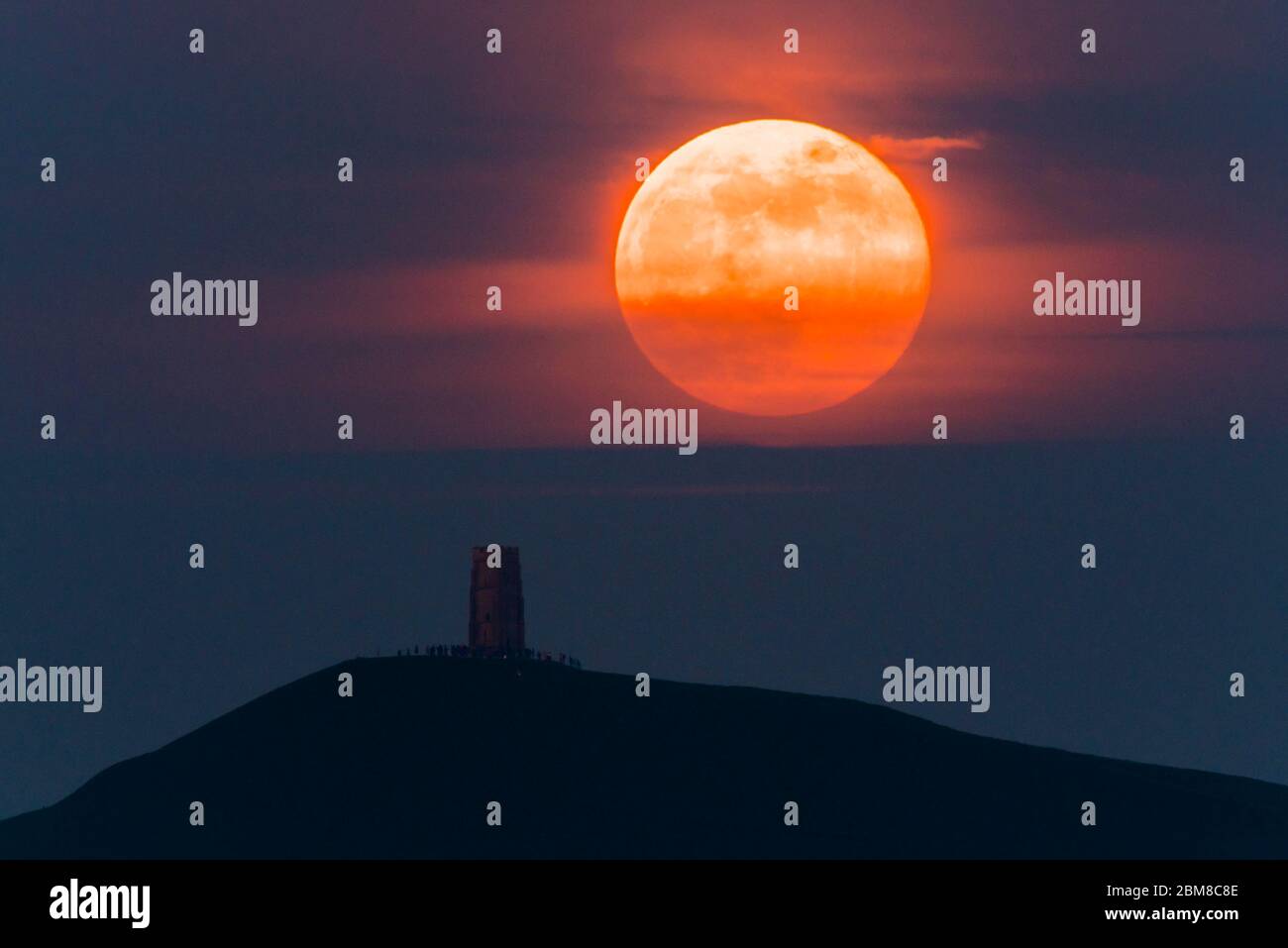 Glastonbury, Somerset, Regno Unito. 7 maggio 2020. Meteo Regno Unito. La luna piena si erge da dietro Glastonbury Tor nel Somerset ma è parzialmente oscurata dalla nuvola che la rende arancione scuro. Questo mese luna è chiamato il fiore luna ed è l'ultima superluna dell'anno. Credito immagine: Graham Hunt/Alamy Live News Foto Stock