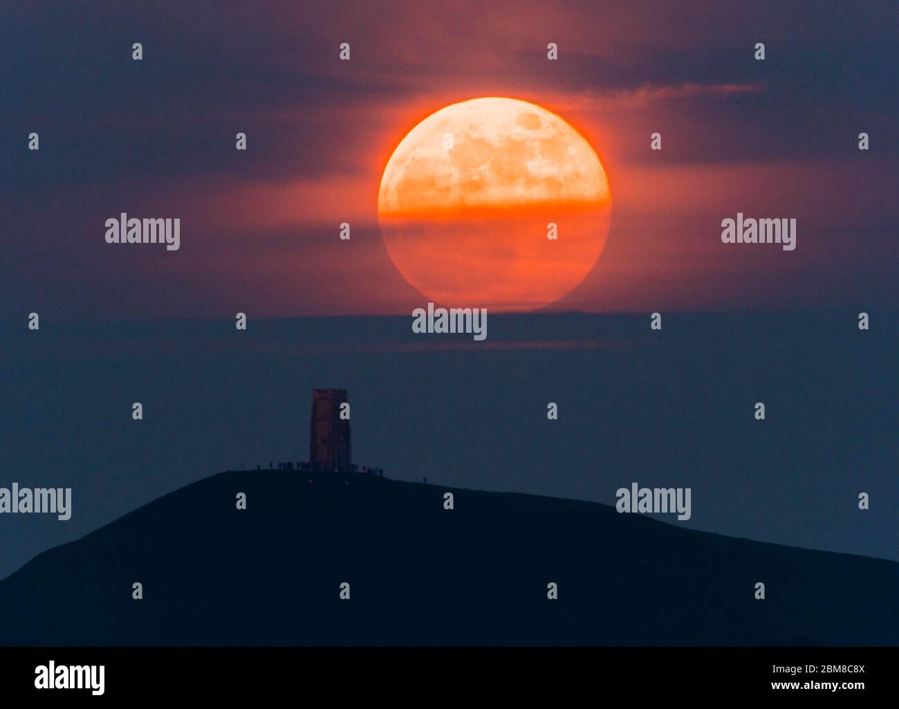 Glastonbury, Somerset, Regno Unito. 7 maggio 2020. Meteo Regno Unito. La luna piena si erge da dietro Glastonbury Tor nel Somerset ma è parzialmente oscurata dalla nuvola che la rende arancione scuro. Questo mese luna è chiamato il fiore luna ed è l'ultima superluna dell'anno. Credito immagine: Graham Hunt/Alamy Live News Foto Stock