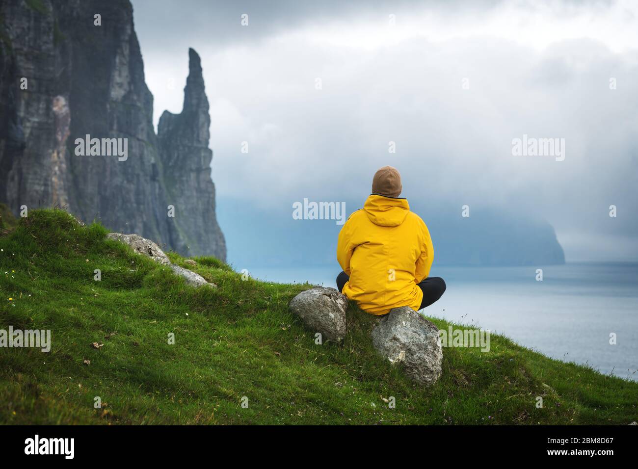Turisti in giacca gialla guarda le streghe scogliere del dito dal punto di vista Trollkonufingur. Funzionario Ministeriale isola, isole Faerøer, Danimarca. Foto Stock