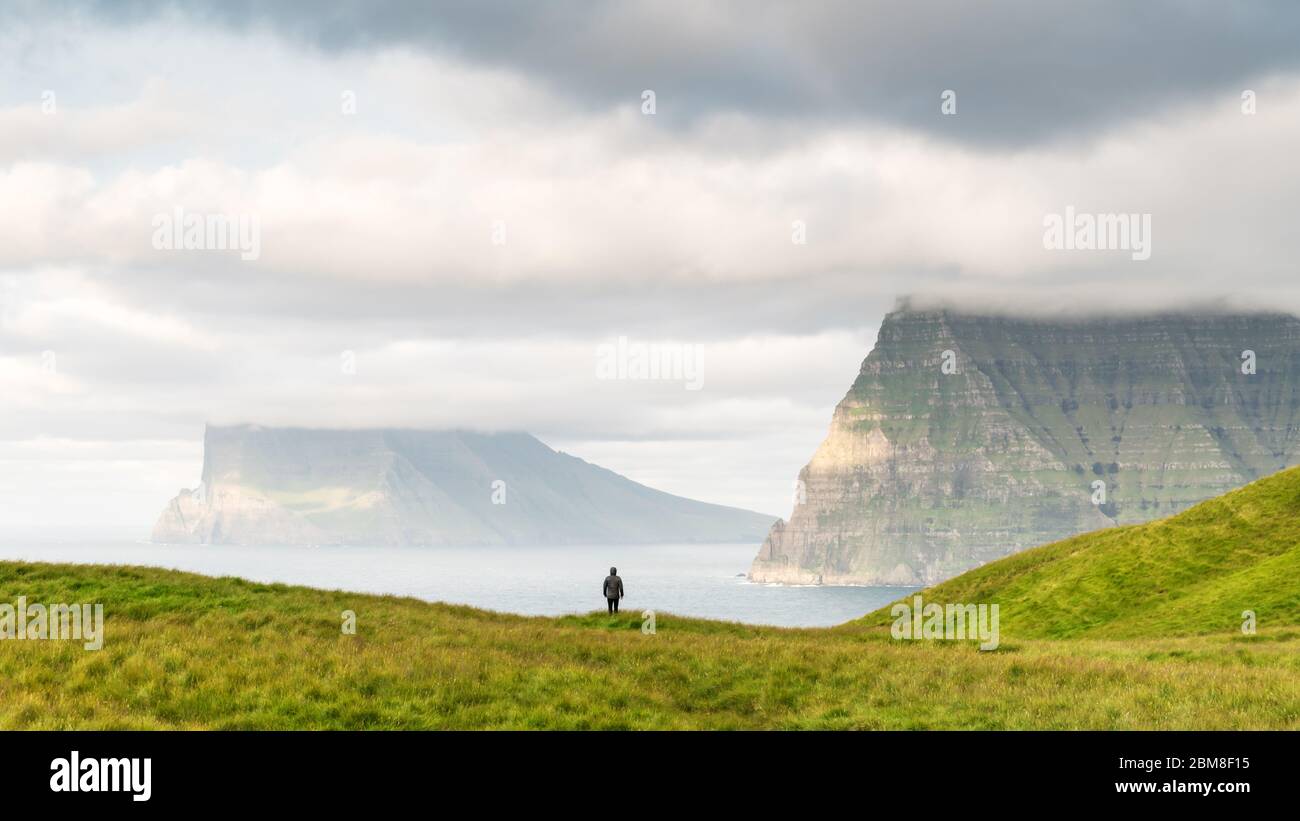 Turista solitario vicino al piccolo lago guarda a foggy isole nell'Oceano Atlantico dalla Kalsoy isola, isole Faerøer, Danimarca. Fotografia di paesaggi Foto Stock