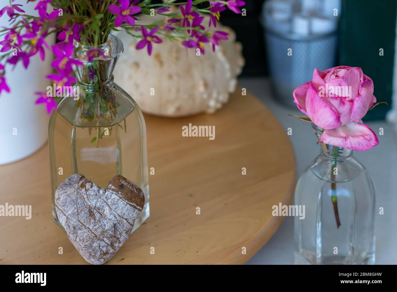 Decorazione interna: angolo casa con rosa, zucca secca, vaso di vetro con fiori selvatici e pietra a forma di cuore Foto Stock