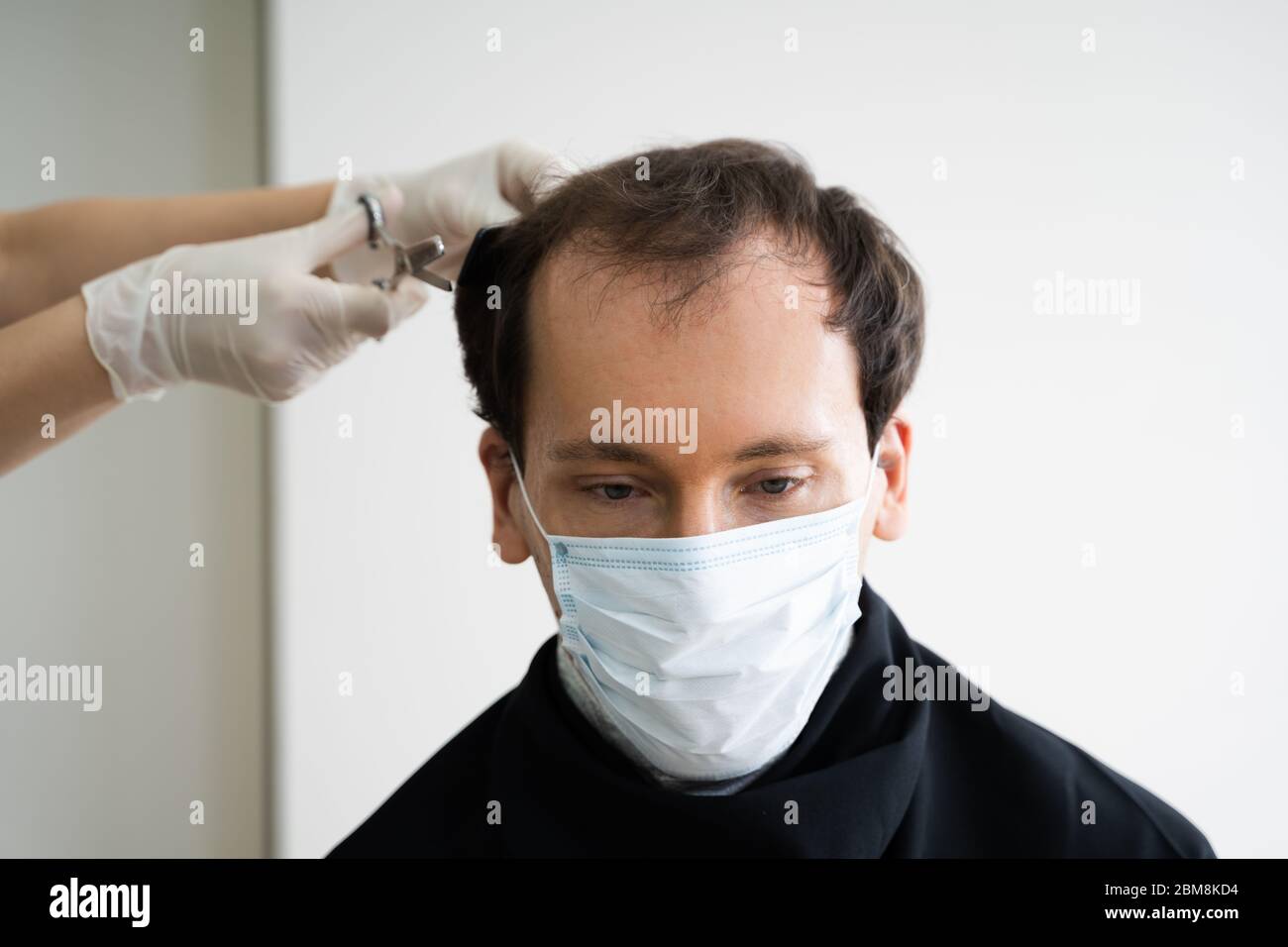 Uomo che taglia i capelli corti al salone in maschera facciale Foto Stock