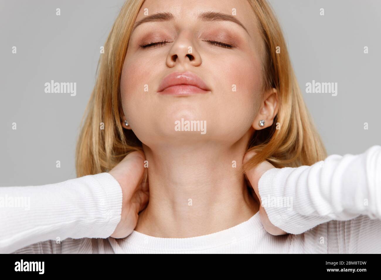 Primo piano ritratto di giovane femmina in bianco top toccare il suo dolore al collo e alla schiena, sente il dolore, massaggi la zona dolorosa. Artrite cervicale, oste Foto Stock