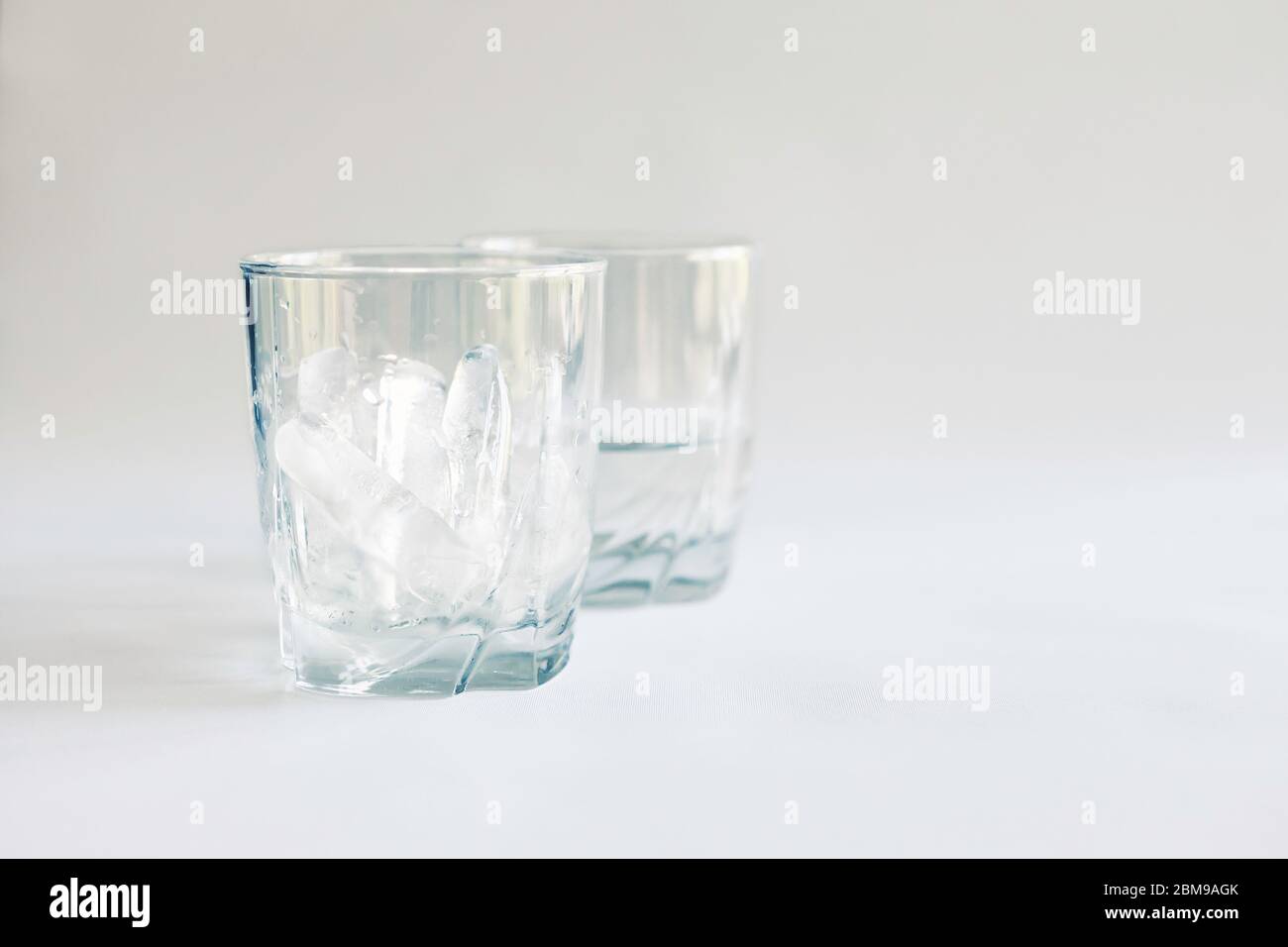 Tumbler pieno di ghiaccio con un secondo bicchiere mezzo pieno di acqua (ghiaccio fuso), Virginia, Stati Uniti, colore Foto Stock