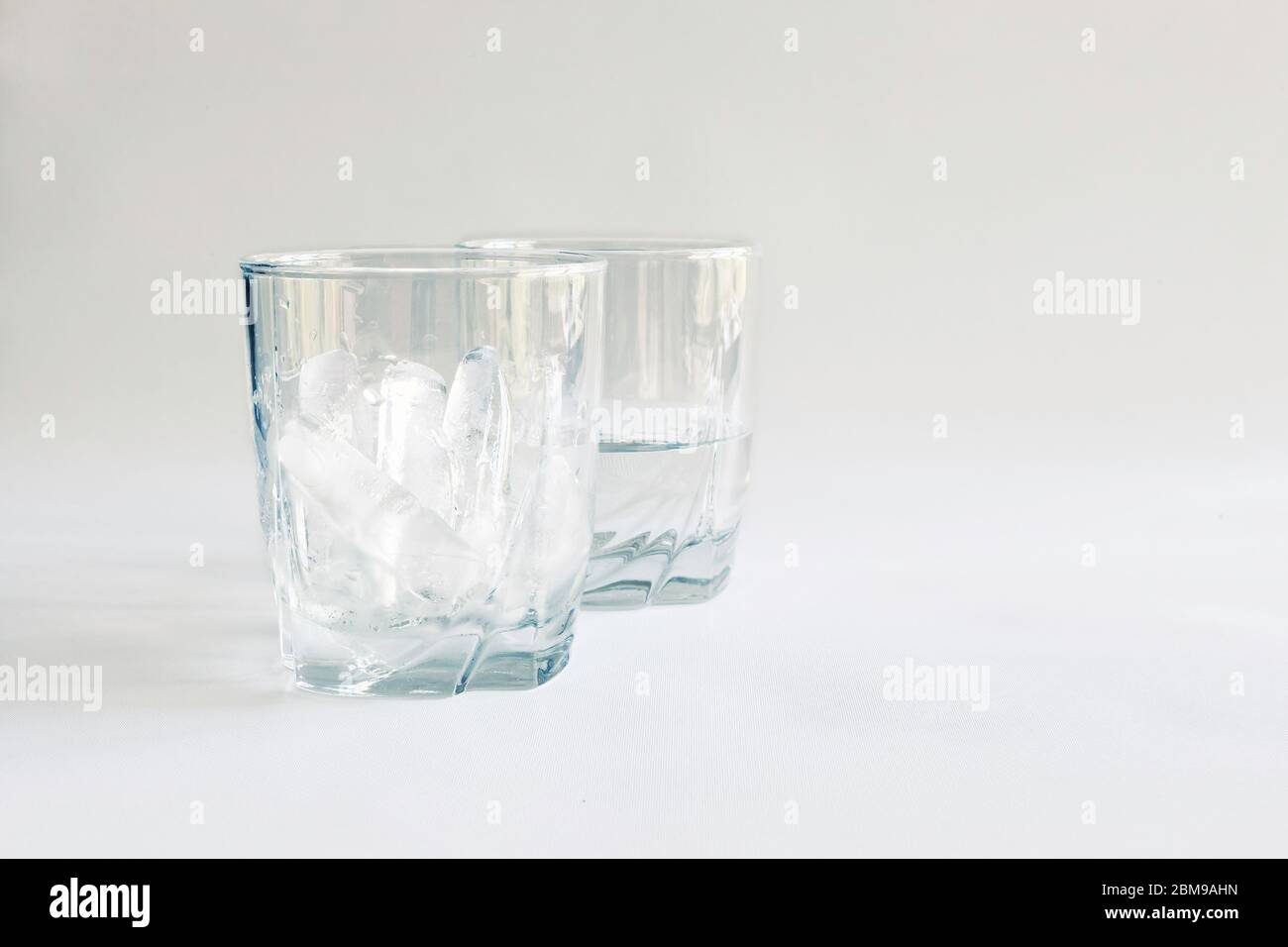 Tumbler pieno di ghiaccio con un secondo bicchiere mezzo pieno di acqua (ghiaccio fuso), Virginia, Stati Uniti, colore Foto Stock