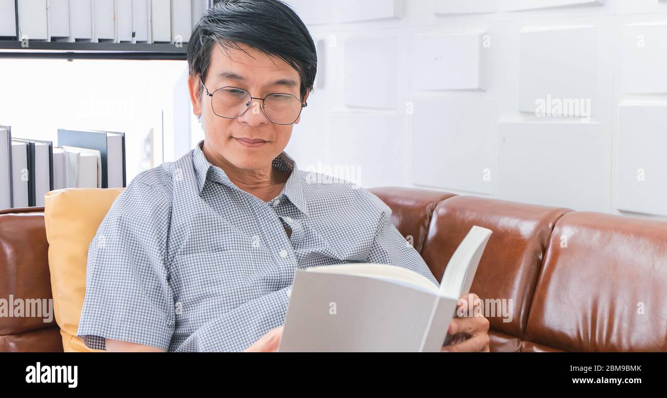 Senior Asian uomo lettura libro sul divano in soggiorno a casa, Ritratto di Asian anziani uomo è rilassante e felicità con Leggi una rivista a casa Foto Stock