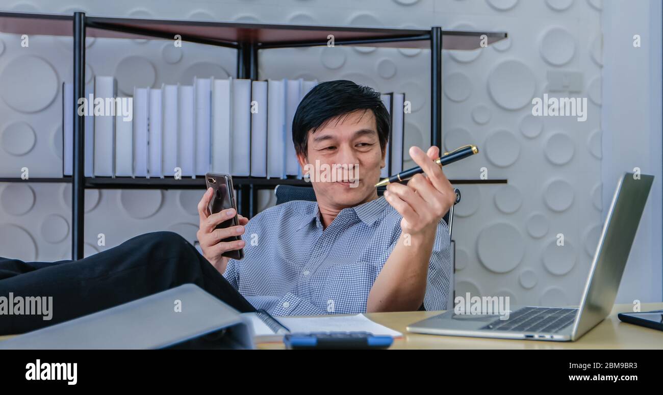 Gli uomini asiatici anziani di affari usano i computer del notebook per il lavoro dalla casa.lui è messo in quarantena nel paese durante l'epidemia di coronavirus. Foto Stock