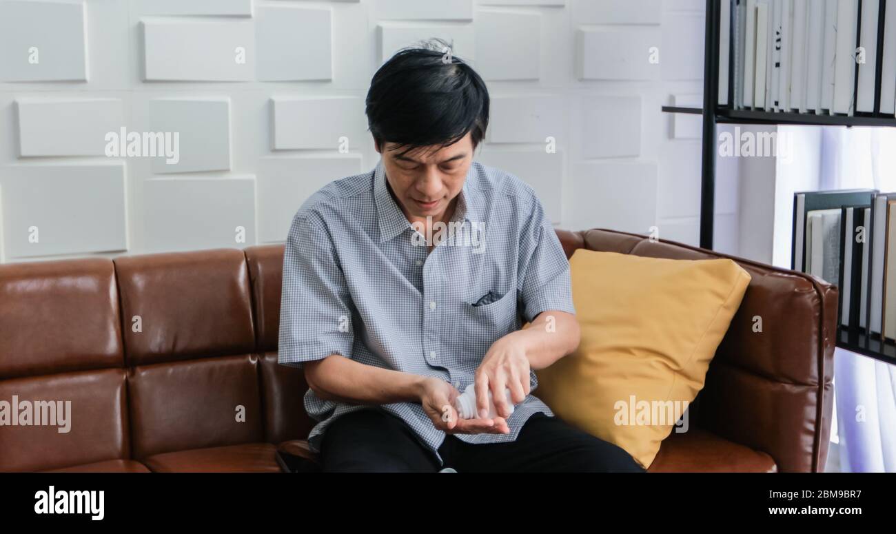 Un anziano asiatico è seduto sul divano e mangiare medicinali per curare la malattia a casa. Foto Stock