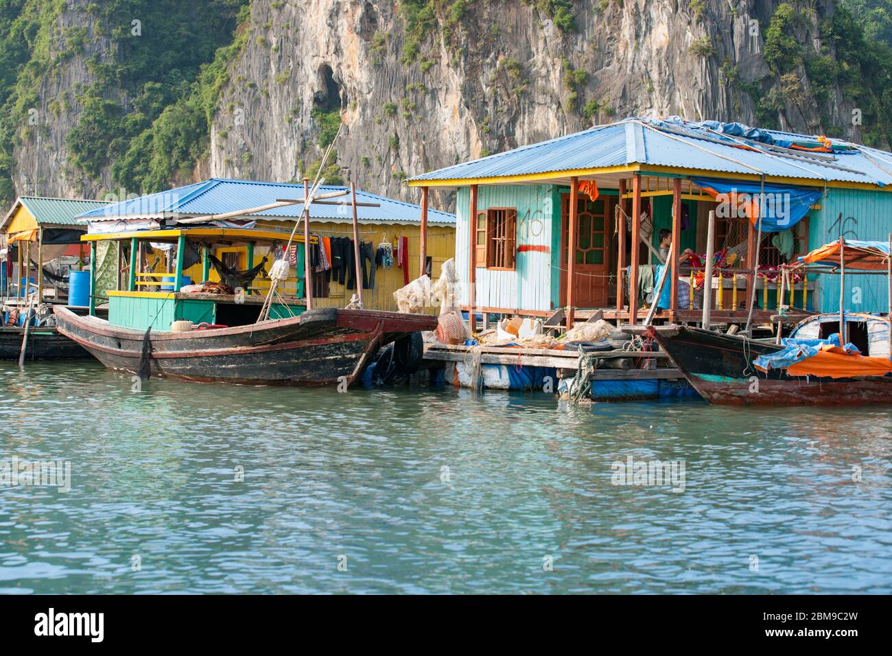 Halong Bay Vietnam - Ottobre 21 2013; case colorate di pescatori costruite sull'acqua contro pareti rocciose con barche da pesca legate alonside. Foto Stock