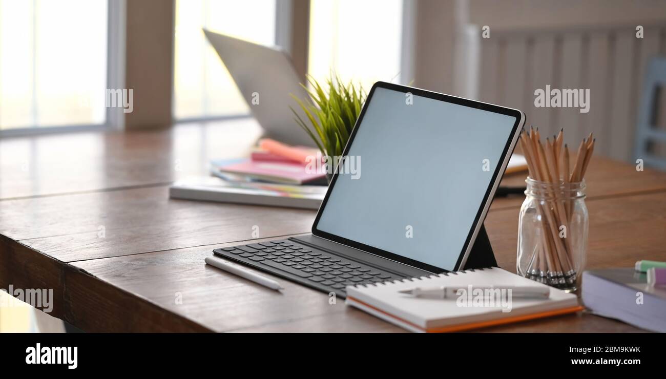 Foto di computer tablet con tastiera porta su scrivania in legno e  circondato da portamatite, notebook, piante in vaso, penna e laptop ove  Foto stock - Alamy