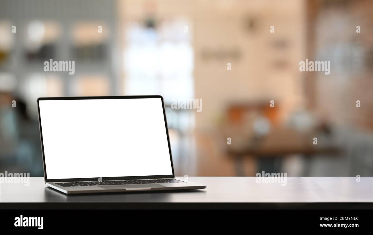 Computer portatile con schermo vuoto che si trova su una superficie liscia scrivania su un comodo soggiorno come sfondo. Foto Stock