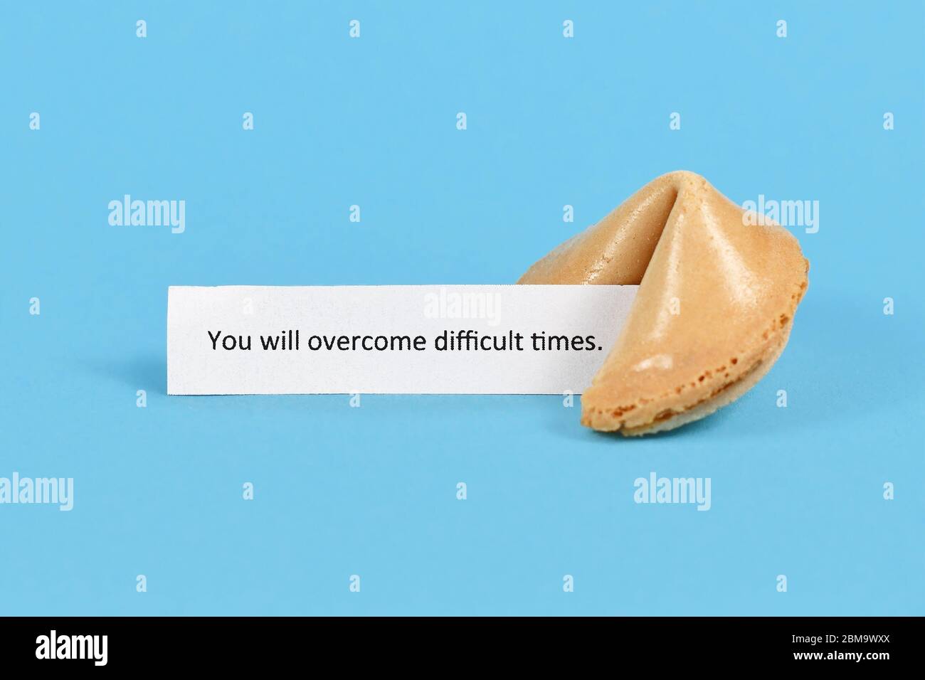 Cookie Fortune con testo motivazionale su carta che dice 'supererete i tempi difficili' su sfondo blu Foto Stock