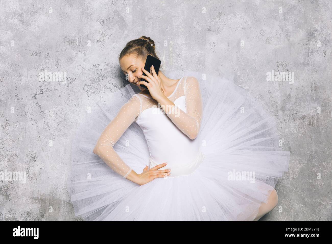 Ballerina giovane ballerina ballerina classica ballerina utilizzando il telefono cellulare contro il muro rustico Foto Stock