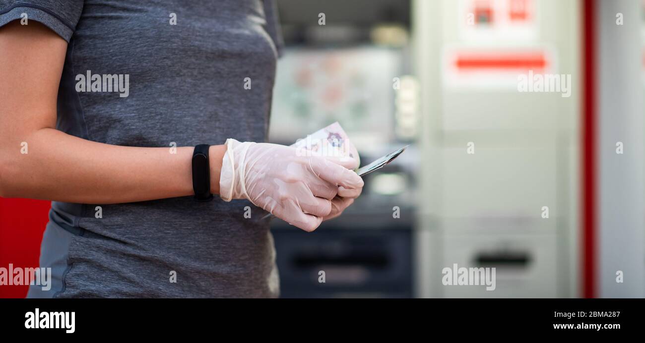 Donna che conta soldi indossando guanti di protezione davanti a un bancomat Foto Stock