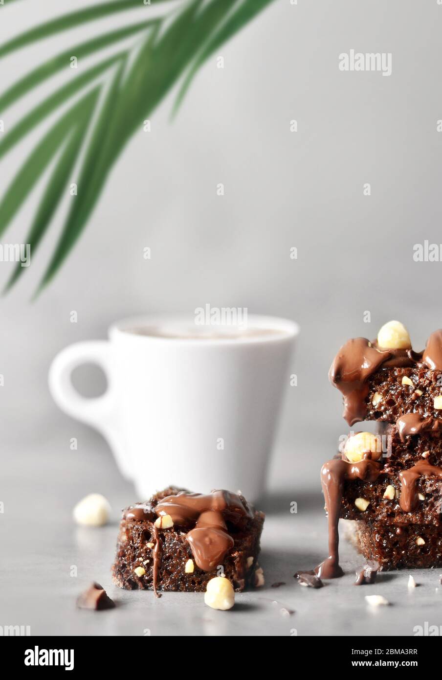 Pila di pezzi di brownie con nocciola, palma e tazza su un tavolo grigio con sfondo grigio. Foto Stock