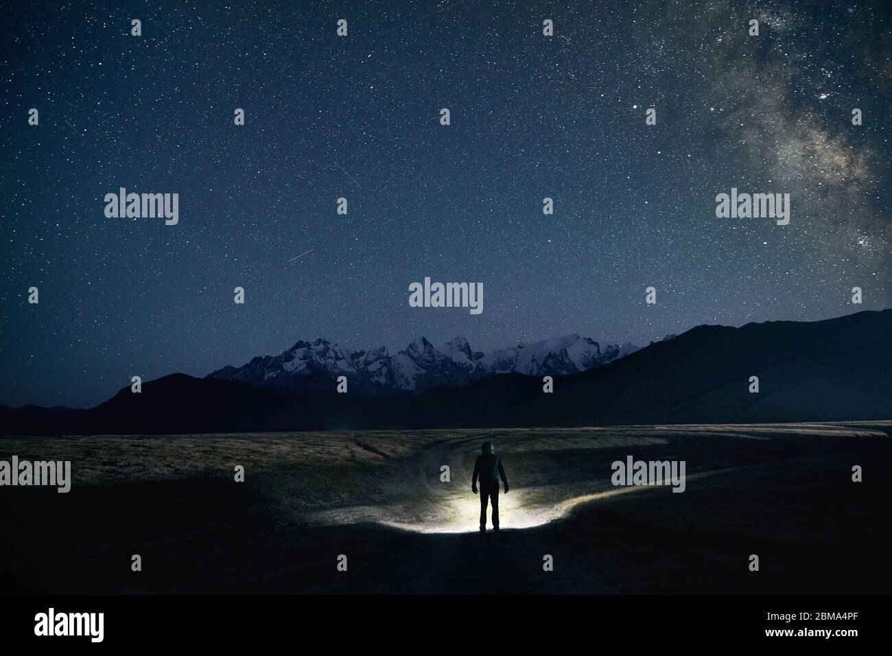 Silhouette dell uomo è la strada di illuminazione con proiettore in montagna sotto il cielo notturno con le stelle. Foto Stock