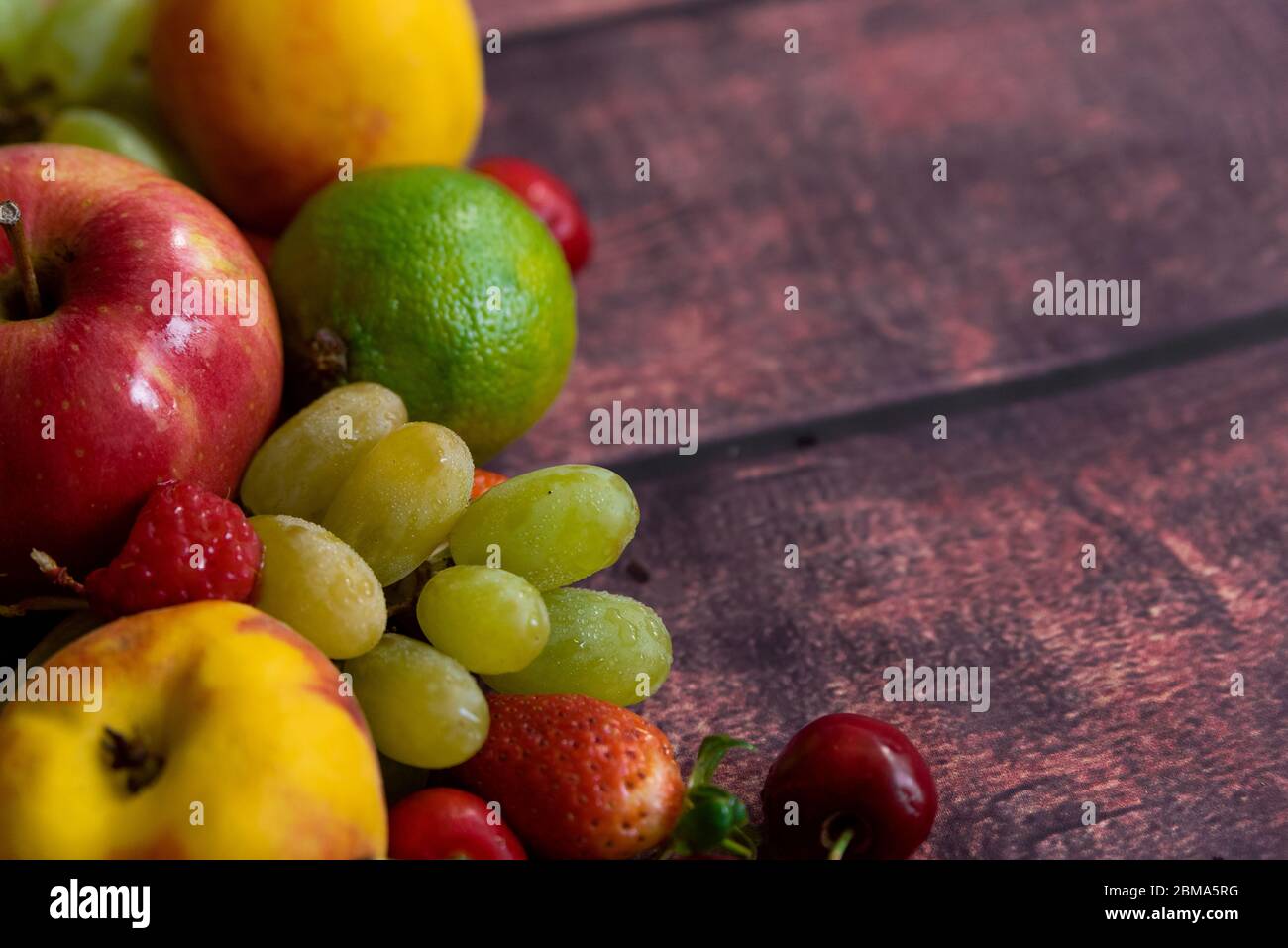 primo piano di frutta primaverile d'uva su tavola di legno con luce naturale, fragole, mirtilli, limone, lime, mela, kiwi, ciliegia, uva, tutto fresco e r Foto Stock