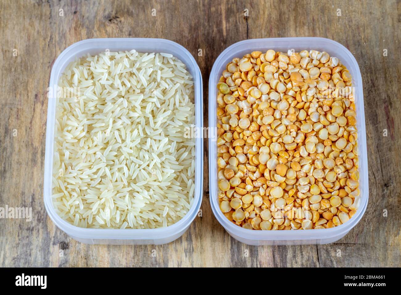 Riso crudo e piselli secchi in contenitori di plastica su fondo di legno Foto Stock