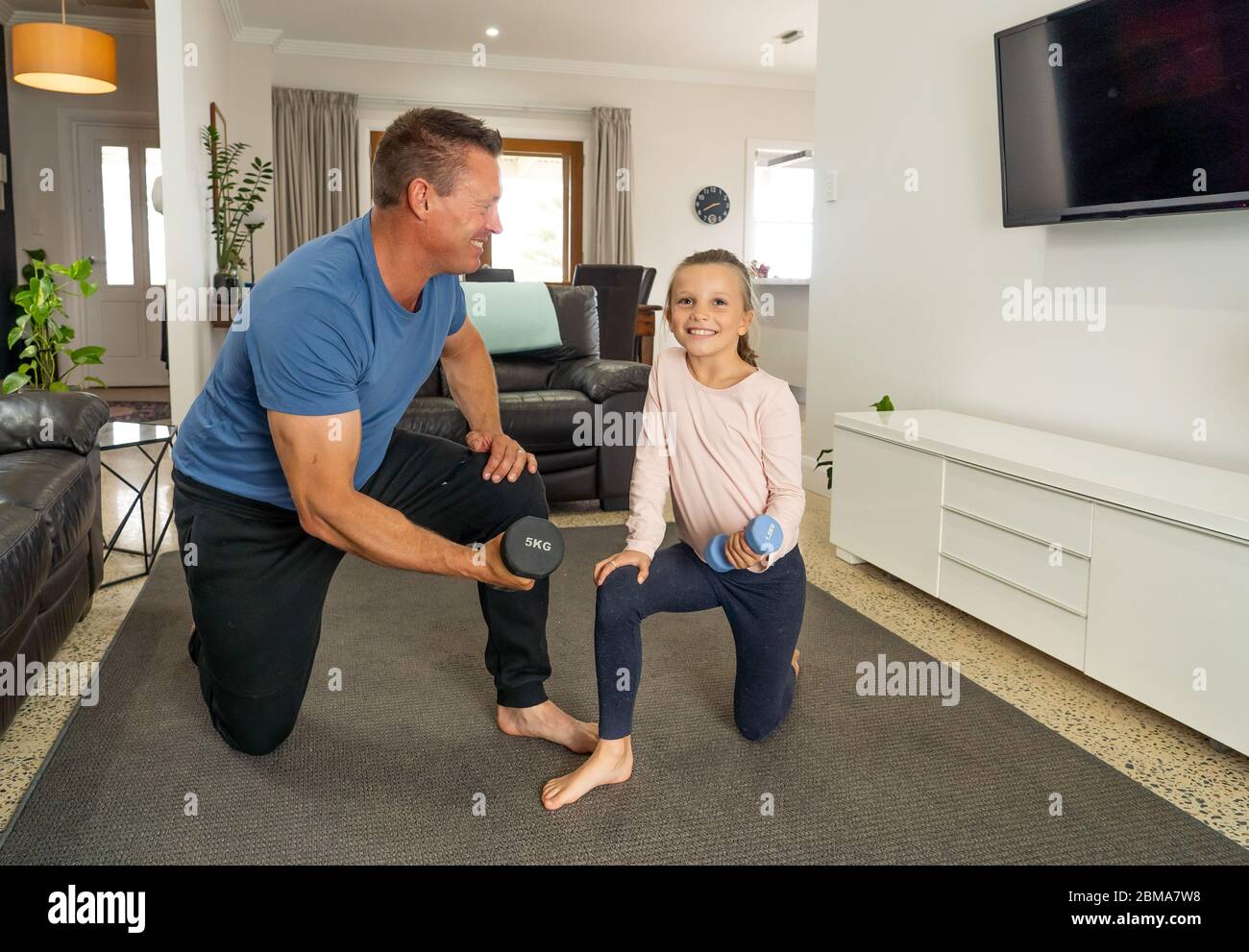 Arresto COVID-19. Padre e figlia in quarantena esercitandosi insieme con dumbbells. Vantaggi dell'attività fisica durante il blocco. Rimani a casa, Foto Stock