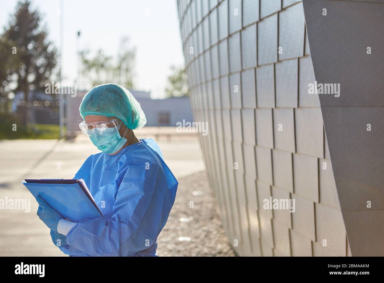Il personale clinico in abbigliamento protettivo tiene la lista dei visitatori di fronte alla clinica a causa di coronavirus e di pandemia di Covid-19 Foto Stock