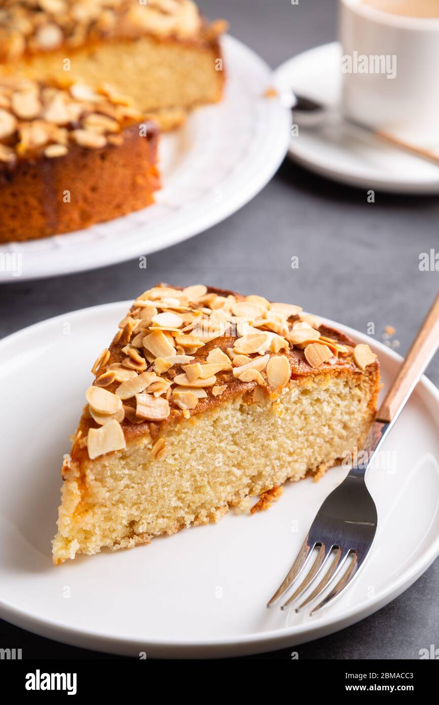 Torta di mandorle e limone con aggiunta di mandorle a fette e una tazza di caffè su una superficie di cemento Foto Stock