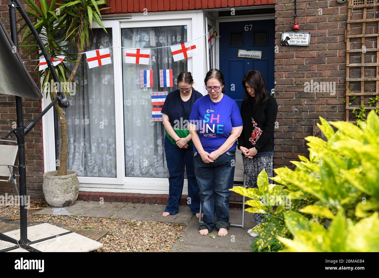 Michelle Martin, 58 (al centro), sua figlia Emma Martin, 37 (a sinistra) e il loro tenente Sara Vottero, 33 (a destra), osservano un silenzio di due minuti a livello nazionale fuori dalla loro casa a Bermondsey, Londra, per celebrare il 75° anniversario della fine del secondo mondo in Europa, rendere omaggio agli eroi passati e presenti. Foto Stock