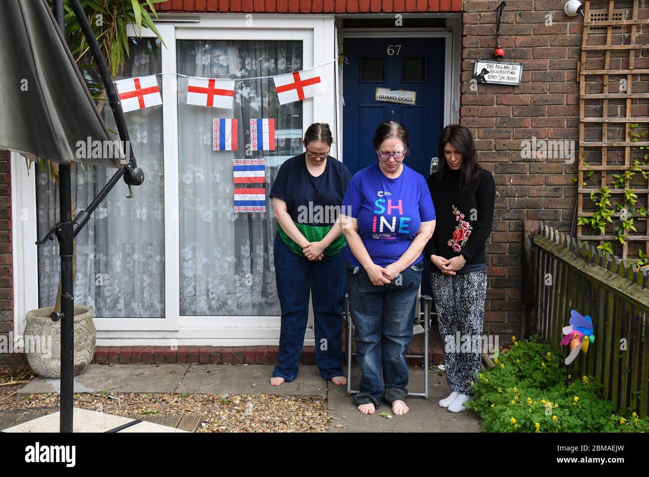 Michelle Martin, 58 (al centro), sua figlia Emma Martin, 37 (a sinistra) e il loro tenente Sara Vottero, 33 (a destra), osservano un silenzio di due minuti a livello nazionale fuori dalla loro casa a Bermondsey, Londra, per celebrare il 75° anniversario della fine del secondo mondo in Europa, rendere omaggio agli eroi passati e presenti. Foto Stock
