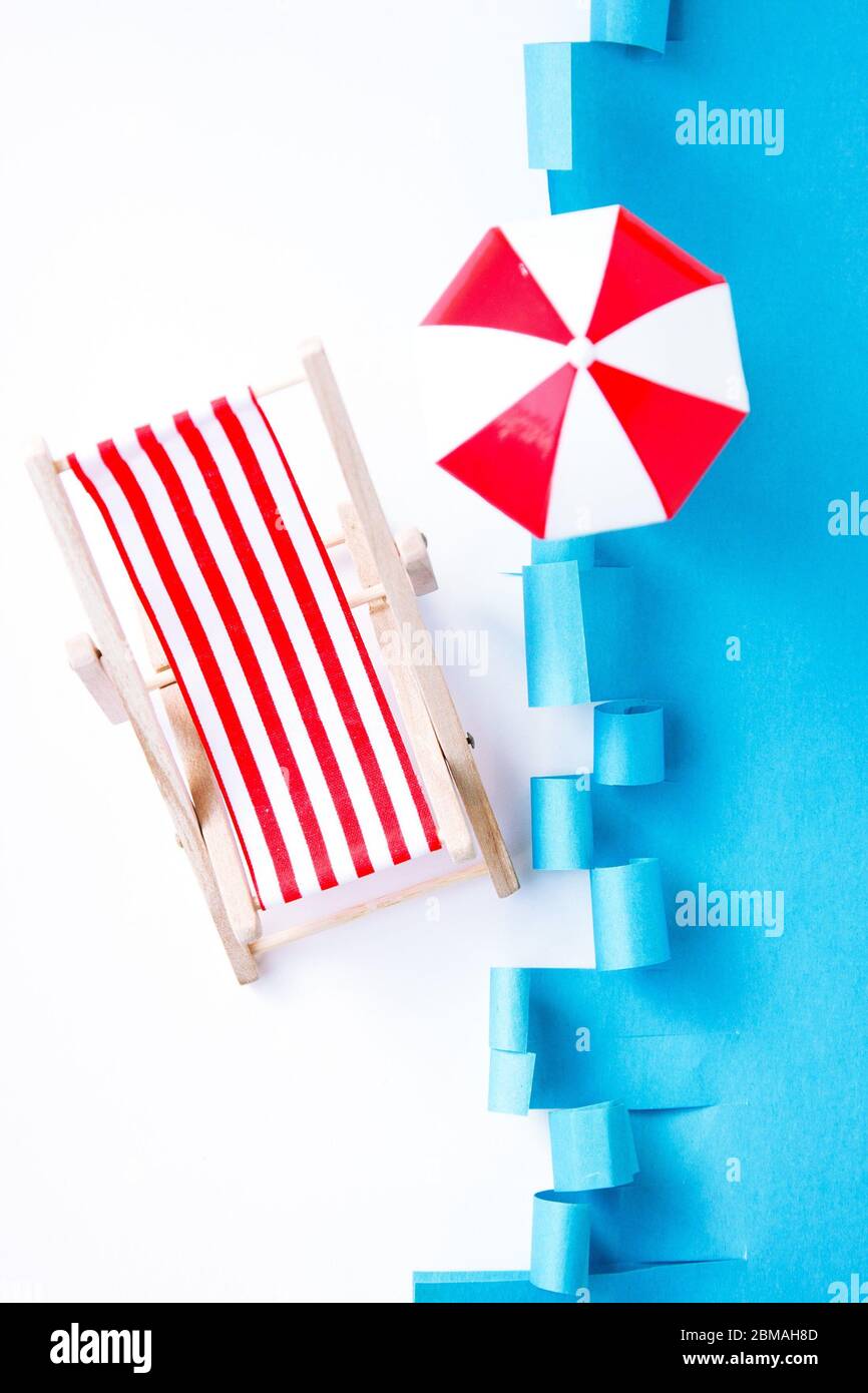 Sedia a sdraio rossa a righe vicino al mare. Sedia reclinabile giocattolo su sfondo blu. Concetto riposo estivo. Vacanze. Foto Stock