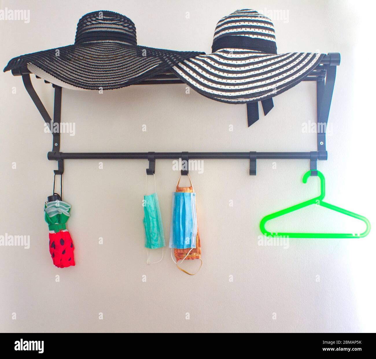 Il concetto di soggiorno a casa. Appendiabiti vuoti e maschera medica protettiva appesi su ganci accanto all'ombrello e cappelli sopra di esso. Foto Stock