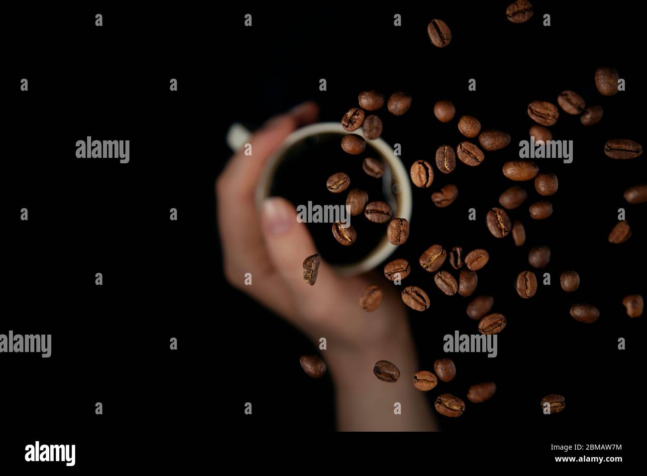 Sorregge con le mani la tazza di caffè con i chicchi di caffè galleggianti, isolati su sfondo nero Foto Stock