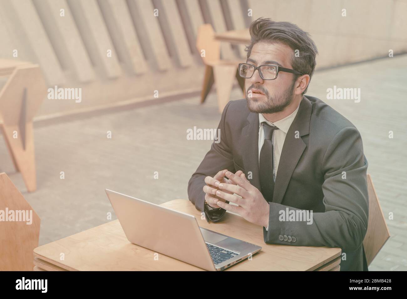 Uomo d'affari che lavora un notebook in strada all'aperto. Giovane uomo intelligente che medita una strategia di sviluppo aziendale mentre si siede al tavolo all'aria aperta Foto Stock