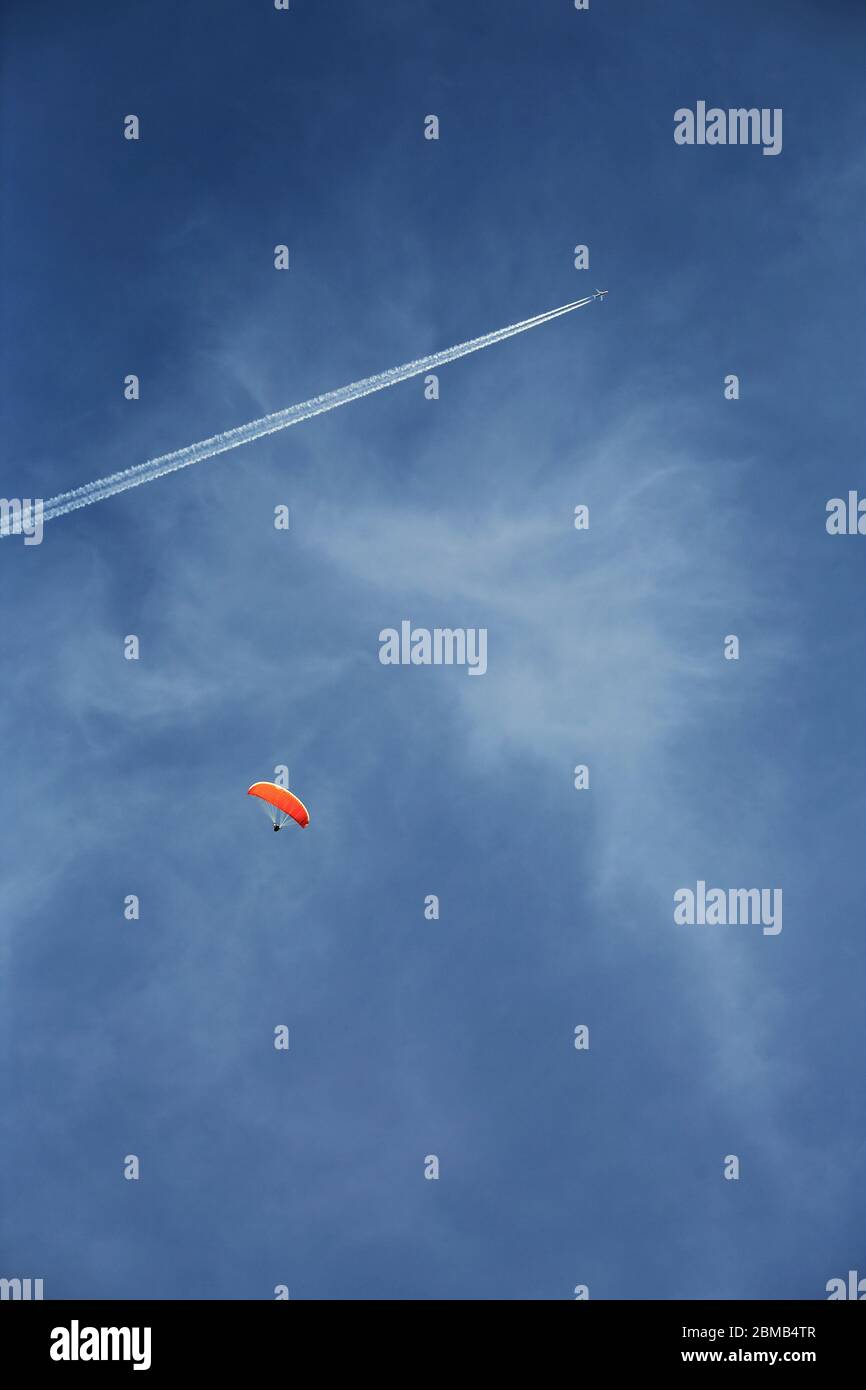Un parapendio con contro un cielo blu, un cirrus nuvole e un aereo commerciale sullo sfondo. Foto Stock
