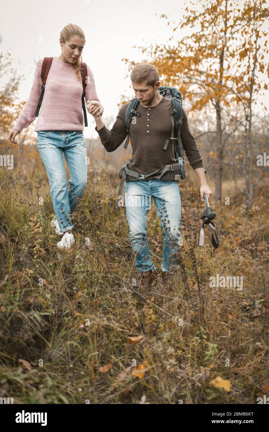 L'uomo sostiene una bella bionda con uno zaino che cammina insieme nella natura selvaggia in autunno Foto Stock