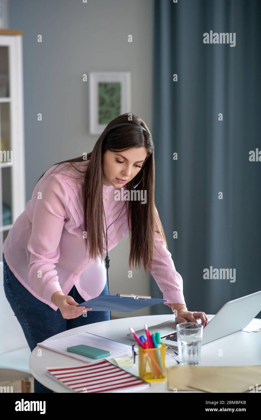Giovane donna in una blusa rosa in piedi al tavolo e guardando occupato Foto Stock