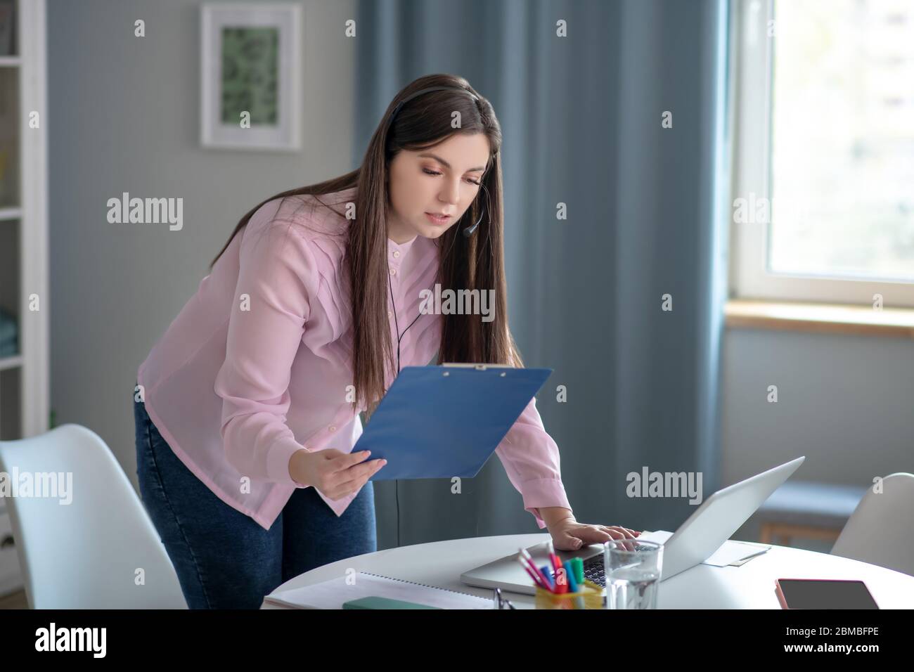 Giovane donna in una blusa rosa in piedi al tavolo e guardando pensieroso Foto Stock