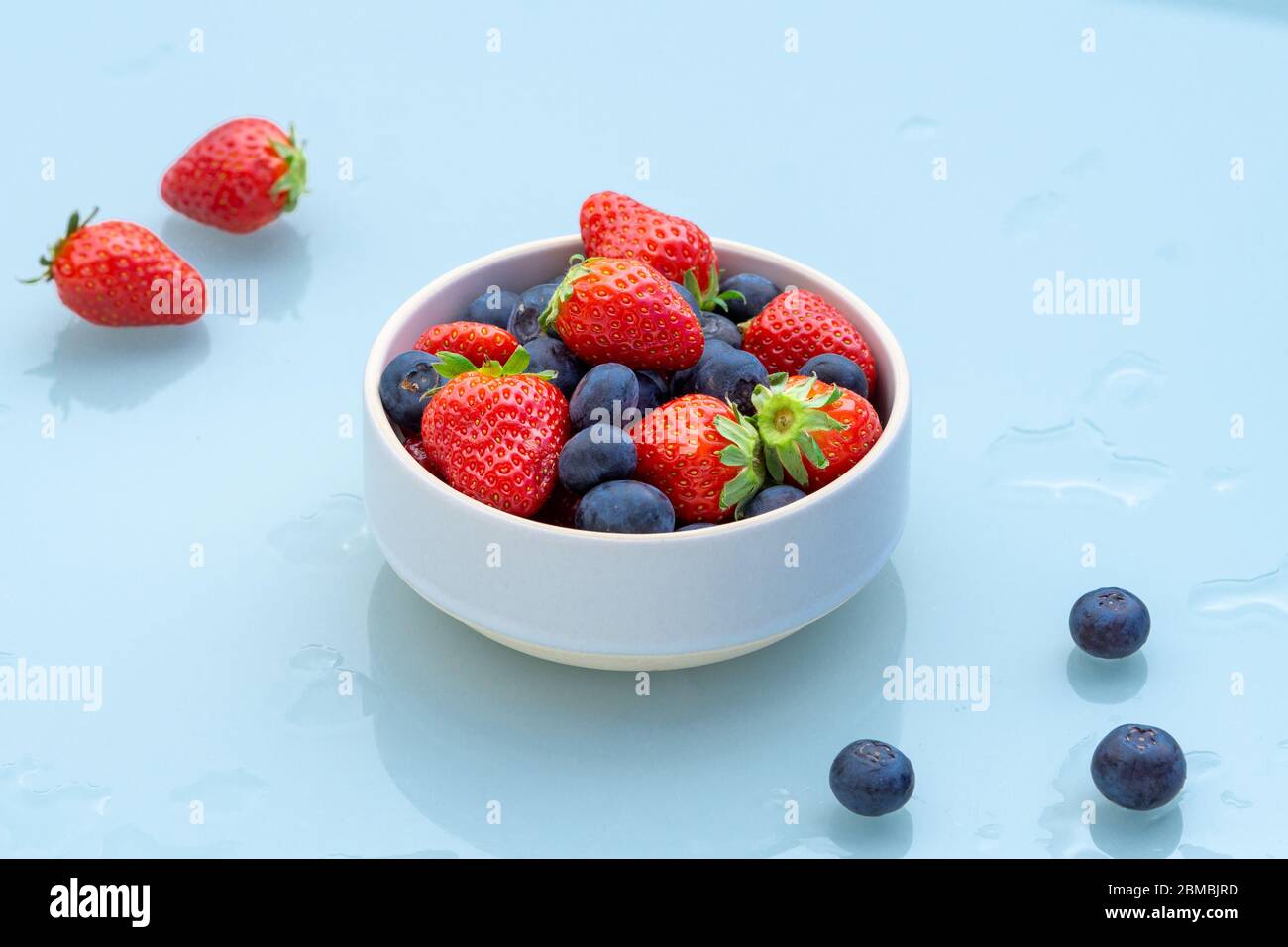 Fragole e mirtilli in una ciotola isolata su sfondo blu. Alcune bacche su un tavolo umido. Primo piano. Sana colazione vegetariana, snack o pasticcio Foto Stock Fragole e mirtilli in una ciotola isolata su sfondo blu. Alcune bacche su un tavolo umido. Primo piano. Sana colazione vegetariana, snack o pasticcio Foto Stock