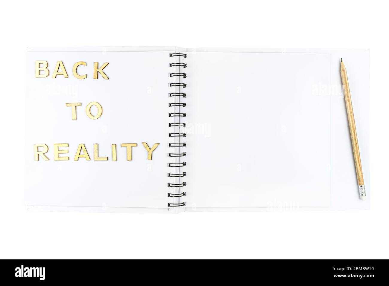 L'iscrizione 'back to reality' è fatta di lettere di legno adagiate su un quaderno aperto con pagine bianche, isolate su sfondo bianco con un PA di ritaglio Foto Stock