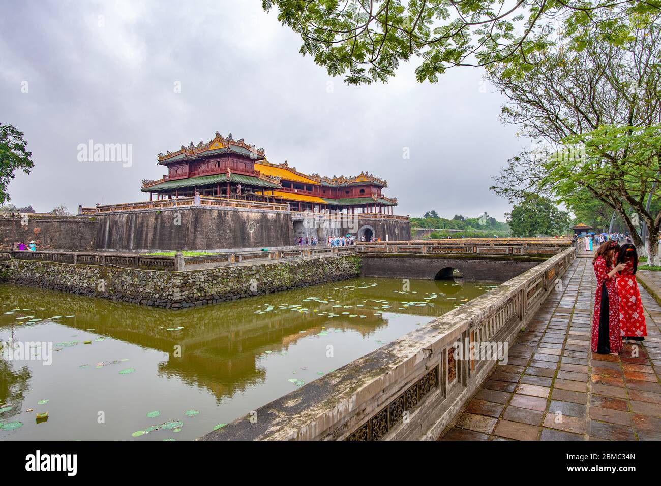 Hue, Vietnam - 15 aprile 2018: Due ragazze che indossano panni tradizionali di fronte alla porta principale della cittadella di Hue, con cielo coperto Foto Stock