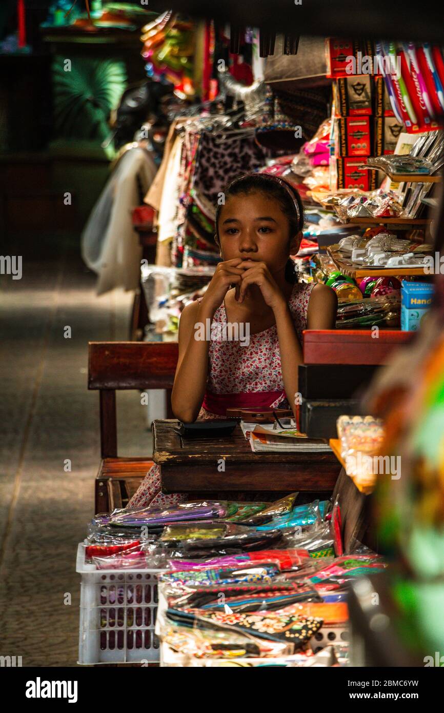 Una giovane ragazza seduta in un mercato di souvenir interno a Hoi An, Vietnam Foto Stock