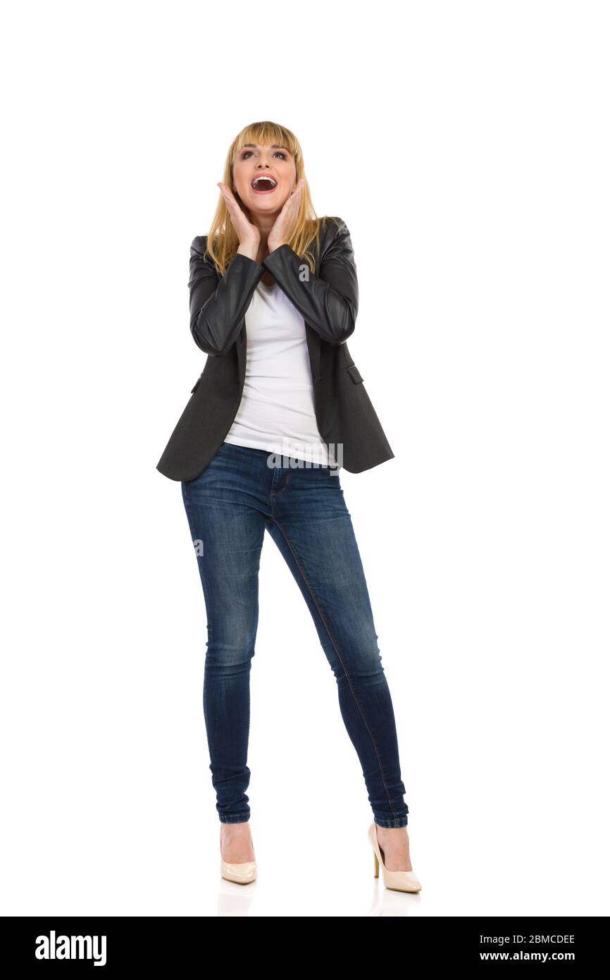 Giovane donna sorpresa in giacca di coda nera senza bottoni, jeans blu e  tacchi alti è
