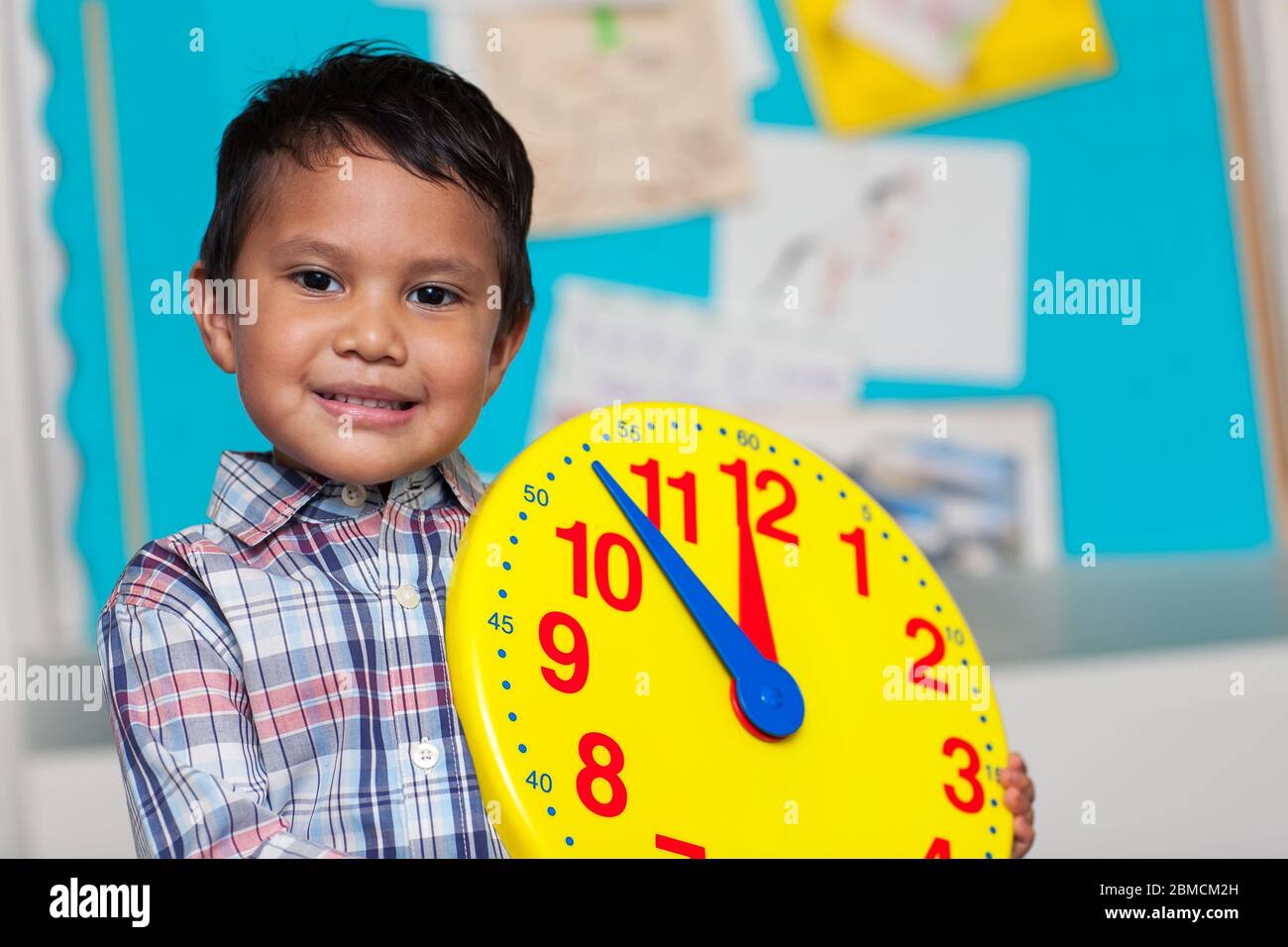 Ragazzo con una camicia preppy, con un grande orologio analogico con un tabellone colorato sullo sfondo. Foto Stock