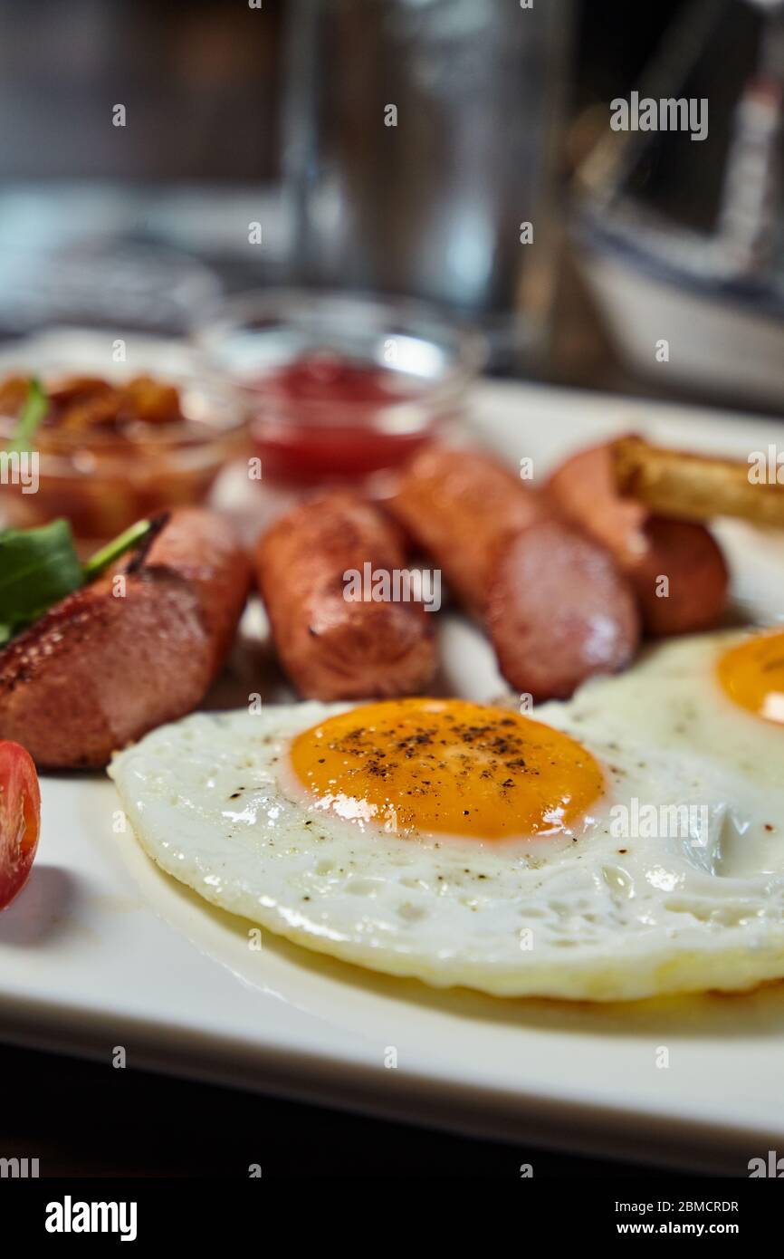Immagine di primo piano della presentazione della colazione: Uova fritte, salsicce e addizioni. Cibo e bevande sfocati Foto Stock