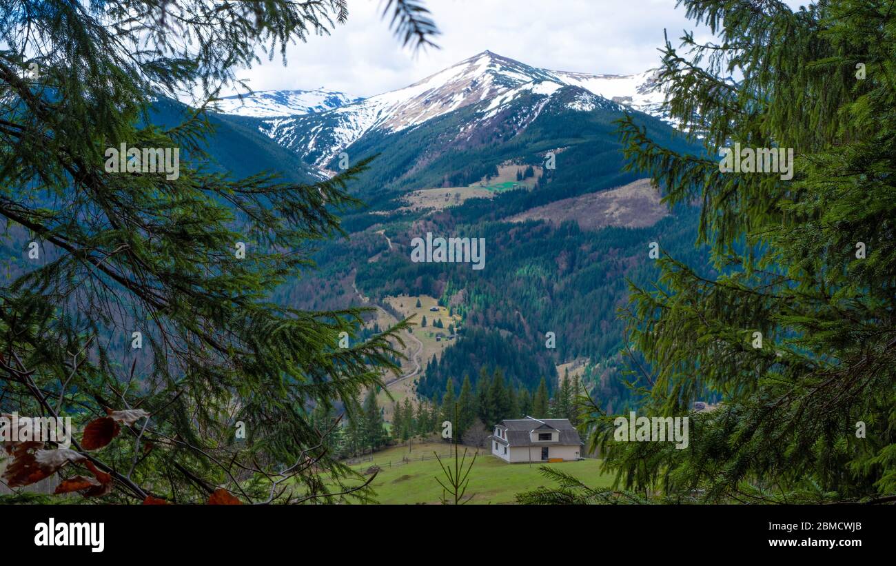 Vista di primavera con montagne blu innevate. Piccolo edificio vicino alle montagne. Ucraina, cresta montenegrina. Foto Stock